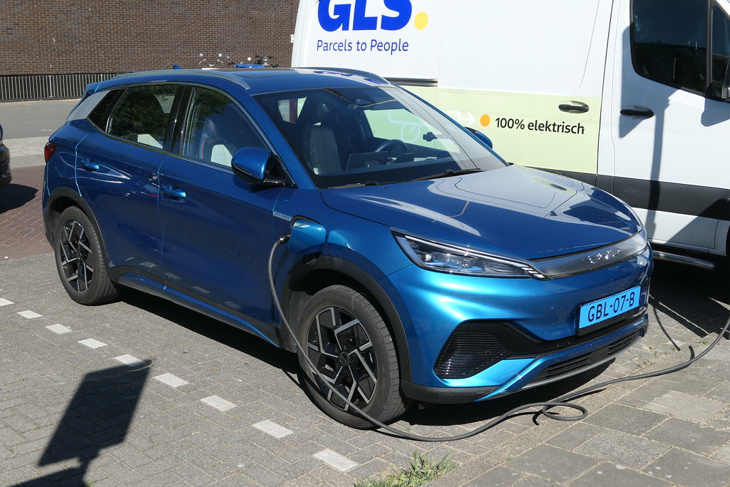Blue BYD Atto 3 electric crossover SUV plugged in for charging, showing front three-quarter view with distinctive headlights and grille.