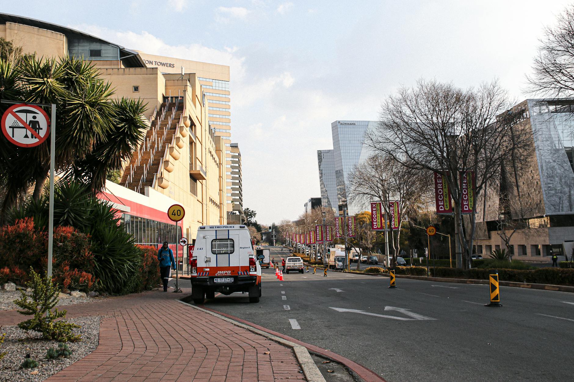 Urban street scene in Johannesburg with office buildings, traffic cones, and a Metro Police vehicle on the road