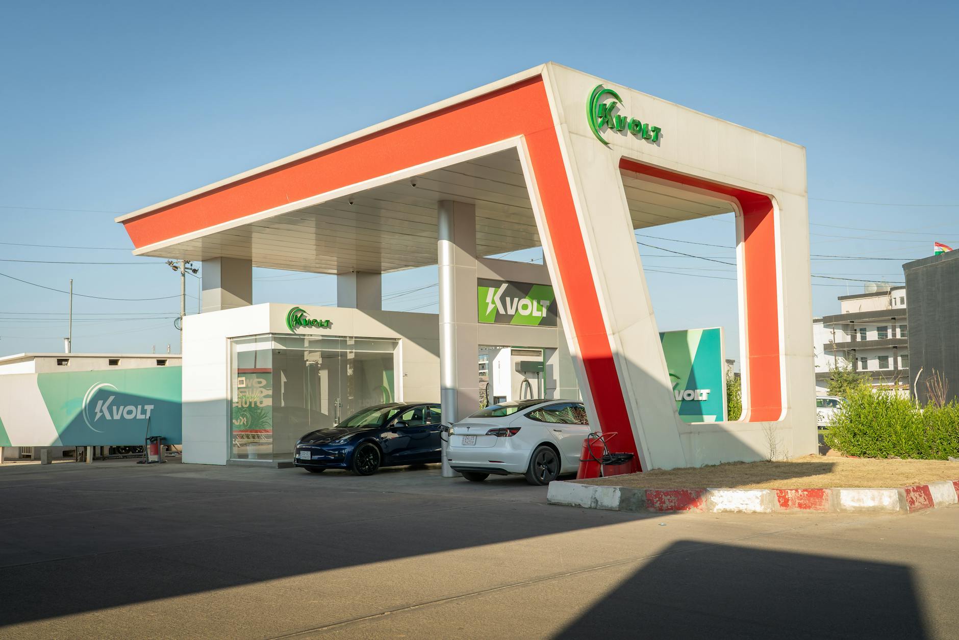 Two electric sedans charging at a modern Kvolt ultra-fast DC charging station with distinctive orange and white canopy architecture.