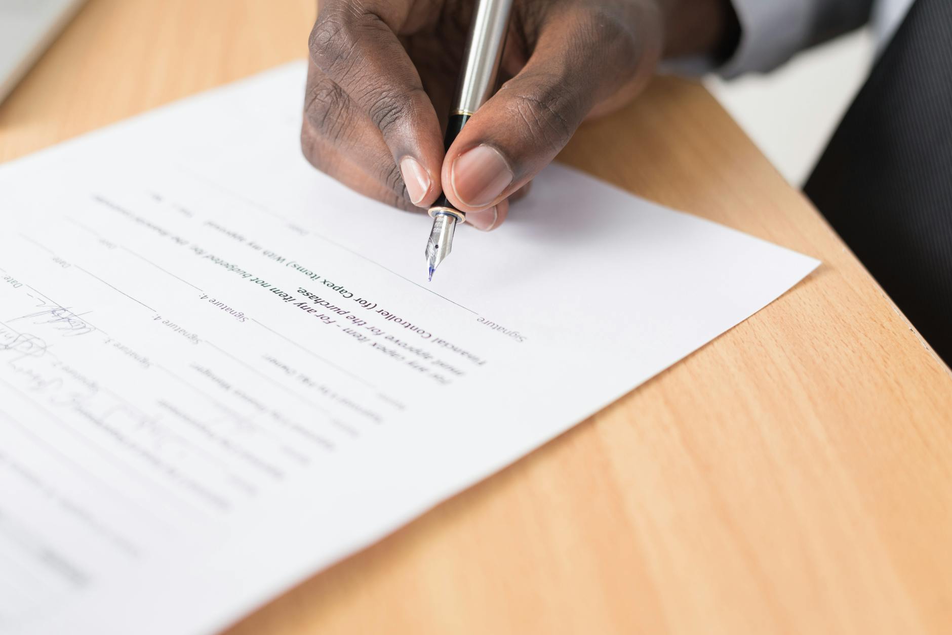 Close-up of hands signing a formal legal document with a fountain pen on a wooden desk