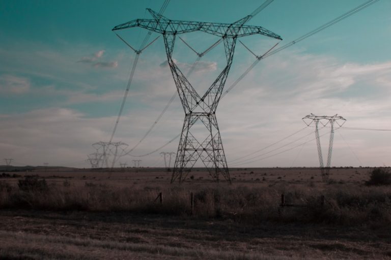 High-voltage transmission towers and power lines stretching across open terrain at dusk
