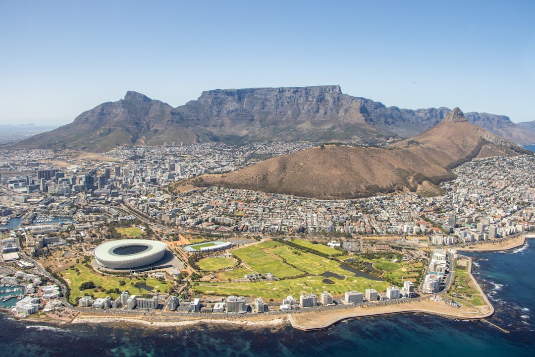Aerial view of Cape Town showing Table Mountain, urban development, Green Point stadium, and Atlantic Ocean coastline.