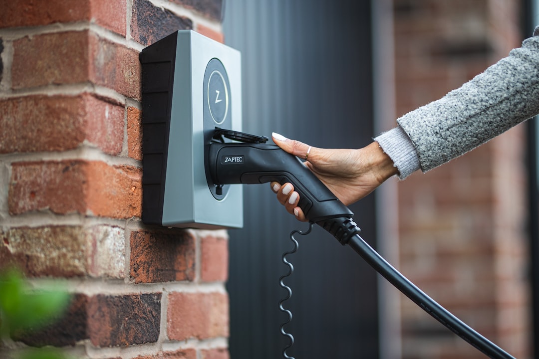 Hand inserting charging cable into wall-mounted Zaptec EV charger on brick exterior wall