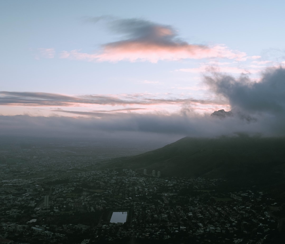 Aerial view of Table Mountain partially shrouded in clouds at dusk, with residential neighborhoods sprawling below