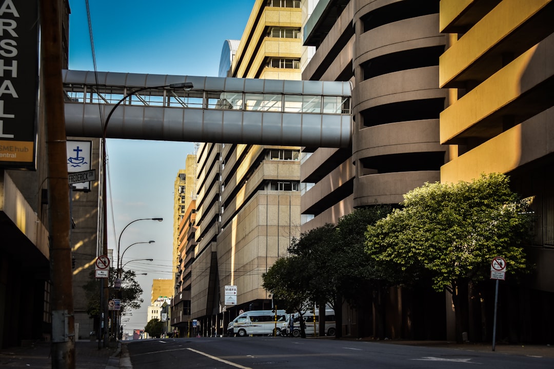 Urban street with modern office buildings, elevated pedestrian walkway, and vehicles on the road during golden hour lighting.