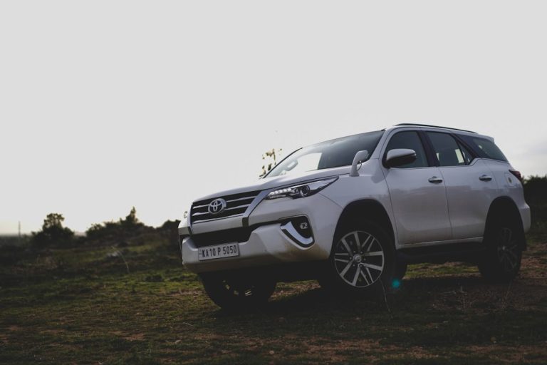 White Toyota Fortuner SUV positioned on dirt terrain with grassy landscape in background, front three-quarter view.