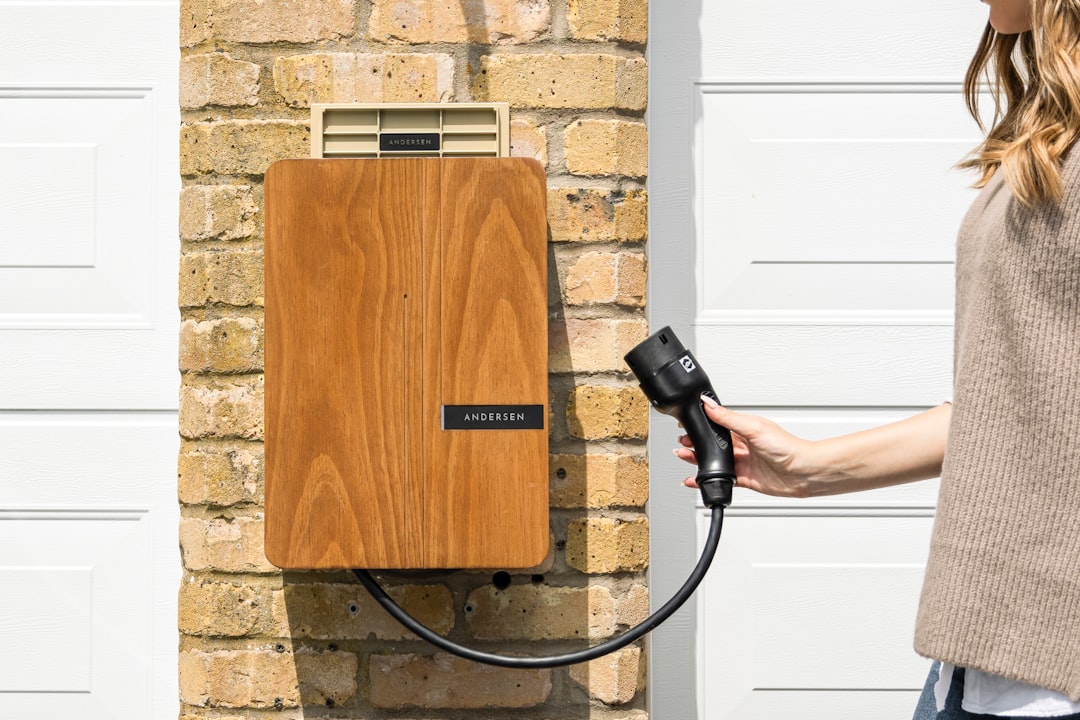 Andersen EV wallbox charger with wooden finish mounted on brick wall, person holding Type 2 charging connector.
