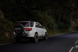White Toyota Fortuner SUV with rear-mounted spare tire driving on a winding mountain road