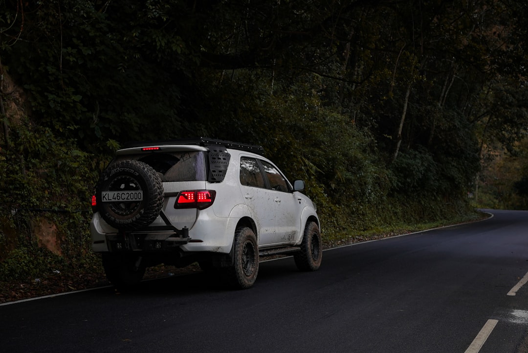White Toyota Fortuner SUV with rear-mounted spare tire driving on a winding mountain road