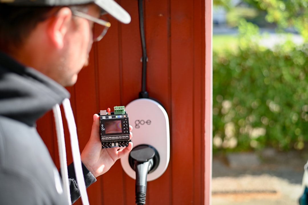 Technician holding a digital electricity sub-meter during installation next to a wall-mounted go-e EV charging unit