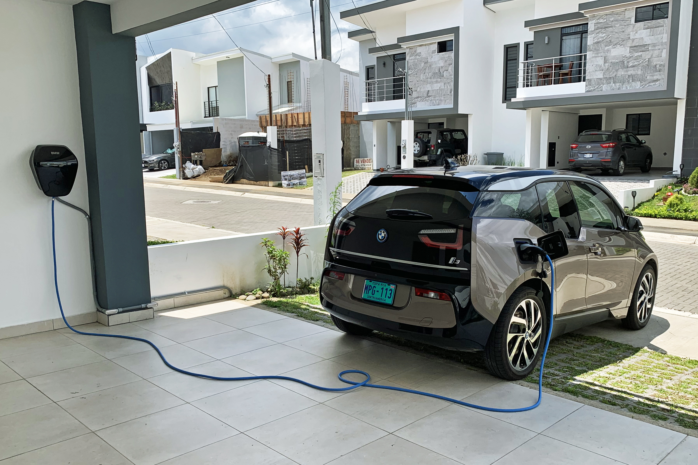 A blue Type-2 cable runs from a home wallbox to a BMW i3 parked in a garage
