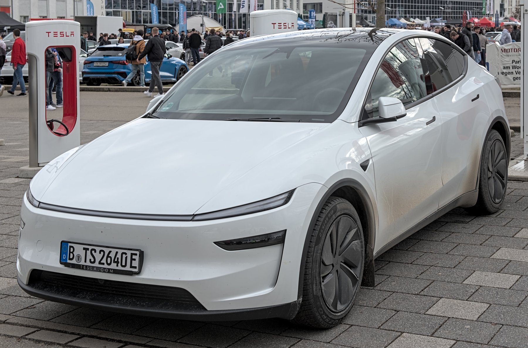 A white 2025 Tesla Model Y parked next to a Tesla Supercharger