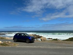 A blue SUV parked by the picturesque coast in Cape Town, South Africa, under a clear blue sky.