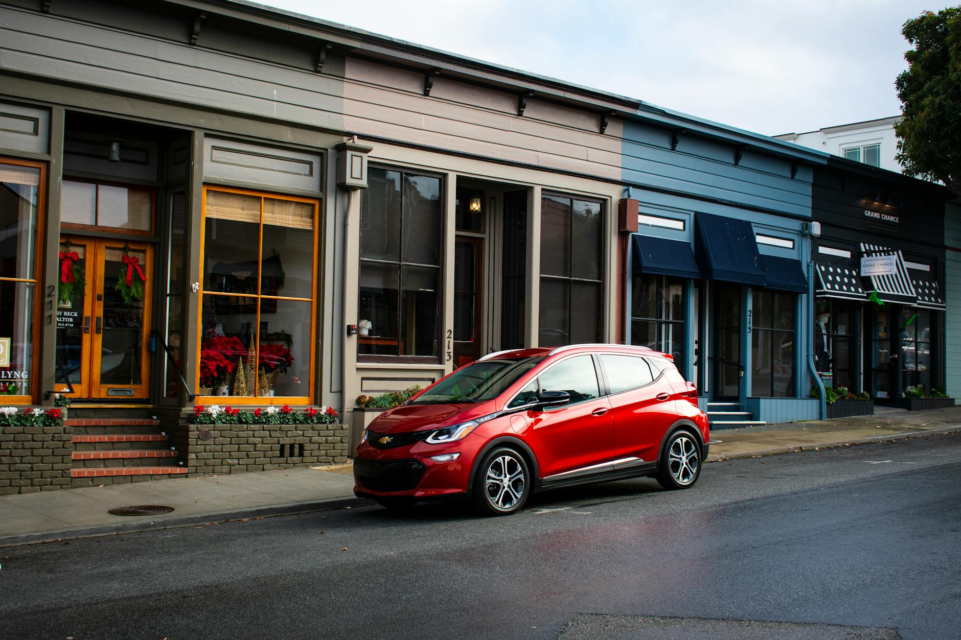 Red electric car parked on a charming street in Pacific Grove, CA, showcasing quaint shops.