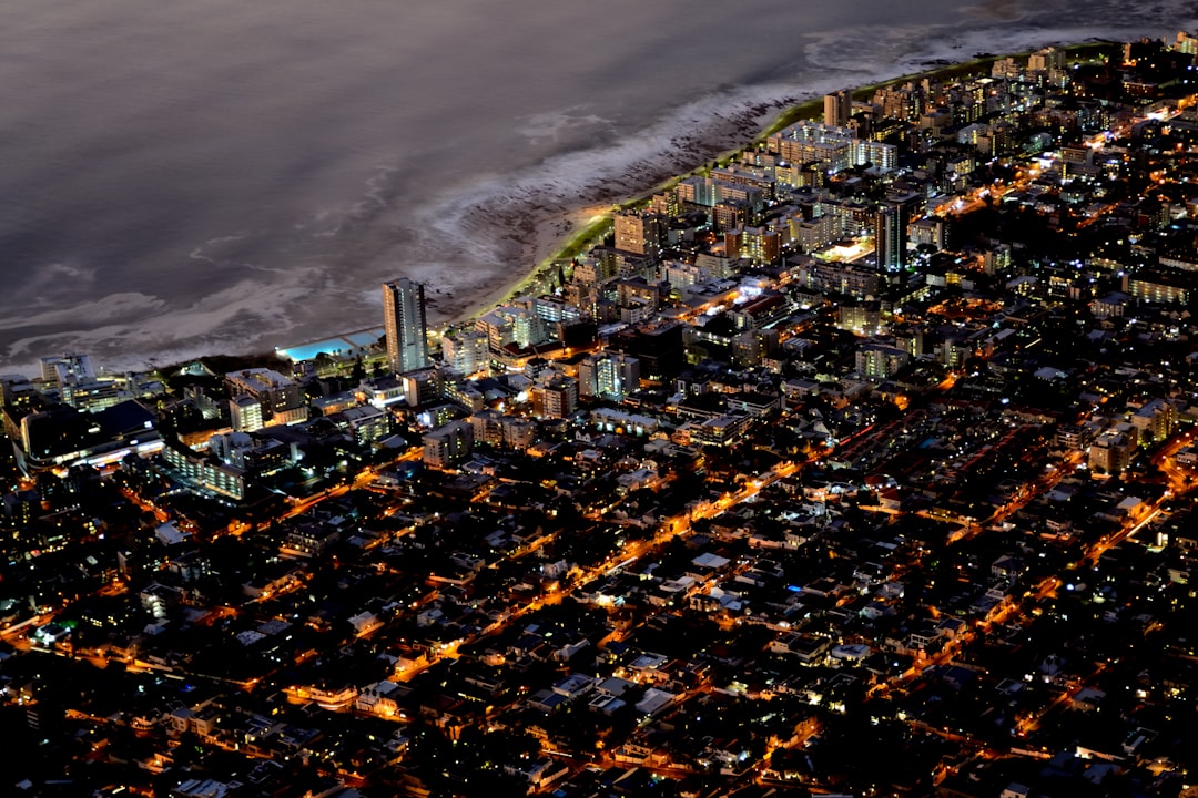 Aerial night view of a coastal suburb with illuminated homes and apartment buildings along a beach, street lights creating orange patterns