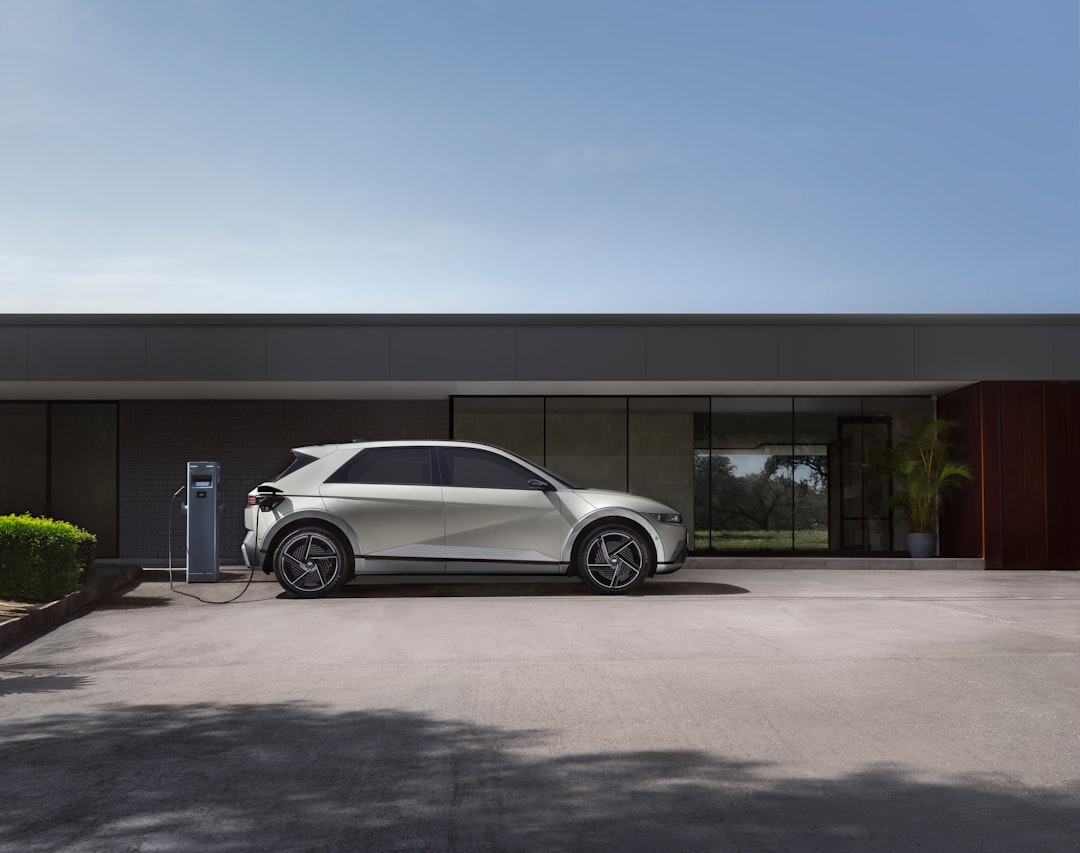 White Hyundai Ioniq 5 electric crossover plugged into a wall-mounted home charger outside a modern residential building