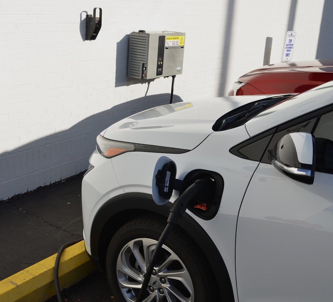 Wall-mounted EV charger with cable connected to white electric vehicle in designated parking space
