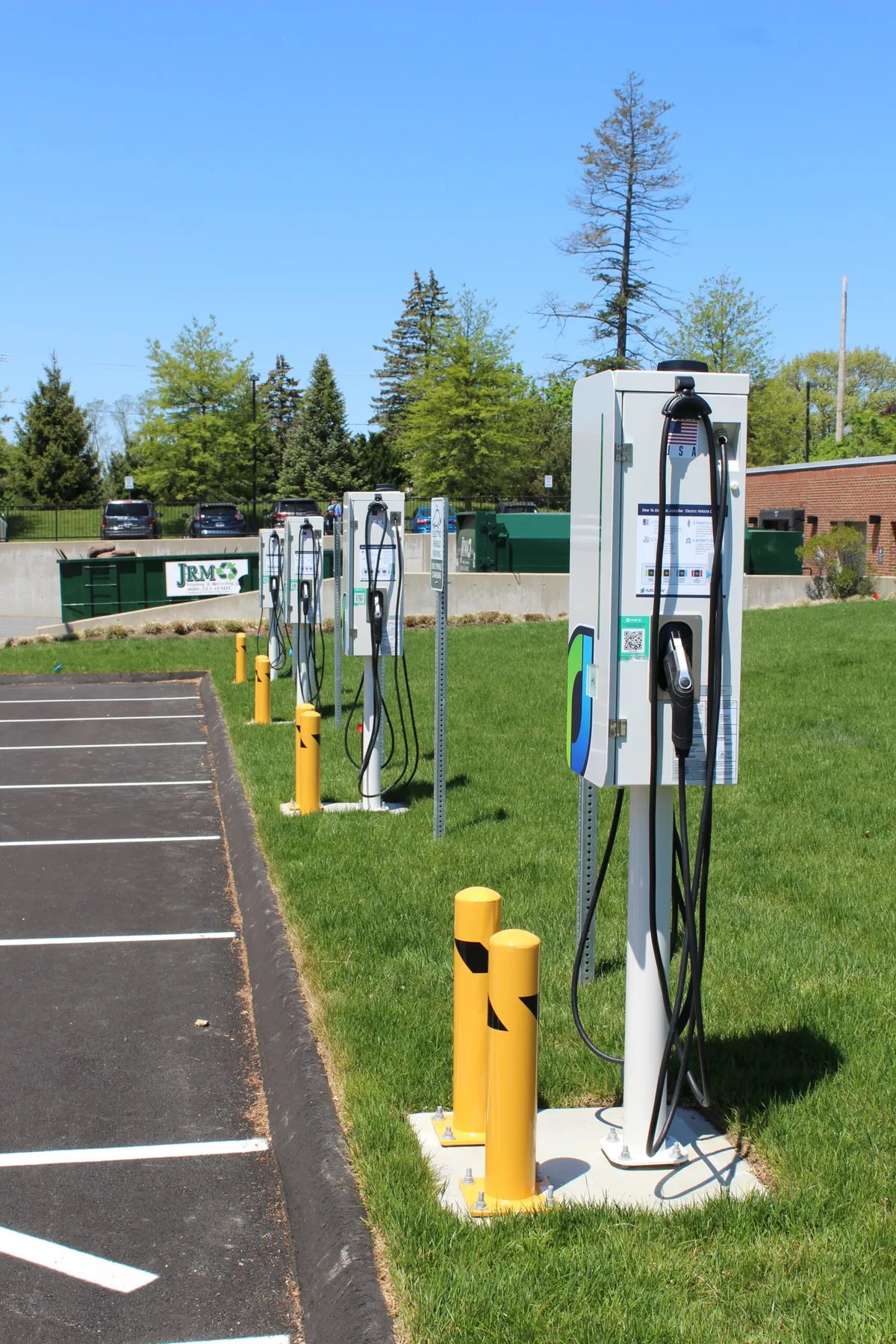 Multiple electric vehicle charging stations with yellow bollards in parking lot, including DC fast charger and AC Level 2 chargers