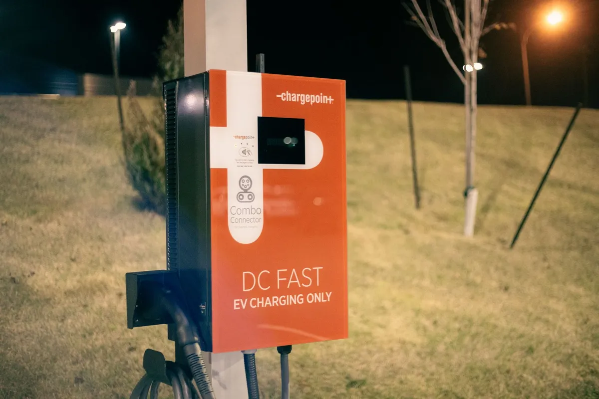 ChargePoint+ DC fast EV charging station at night with orange and white branding, Combo Connector display, lit by surrounding landscape lighting