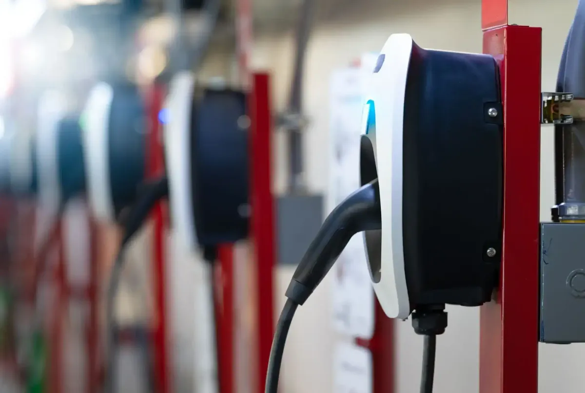 Multiple white and dark EV charging units mounted on red pedestals in a row, with black charging cables attached, showing a bulk deployment installation.