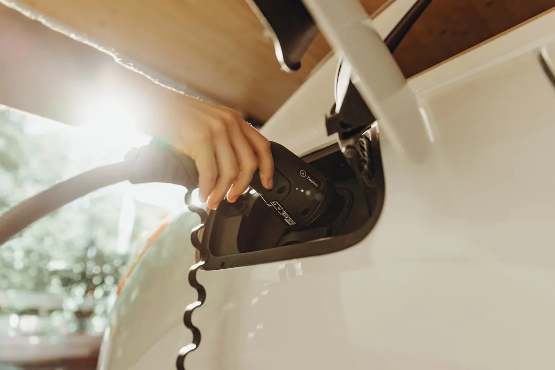 Hand inserting white EV charging cable into vehicle's charging port