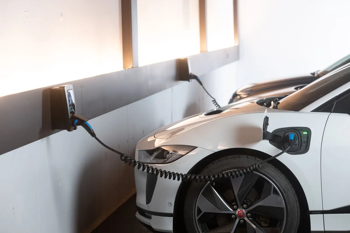 White electric vehicle charging at wall-mounted EV charger on contemporary residential building exterior
