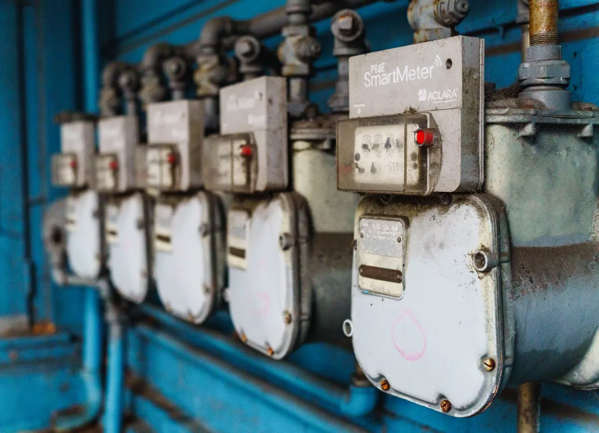Row of residential electricity smart meters mounted on blue metal frame, with one ACLARA SmartMeter prominently focused in foreground showing red indicator light