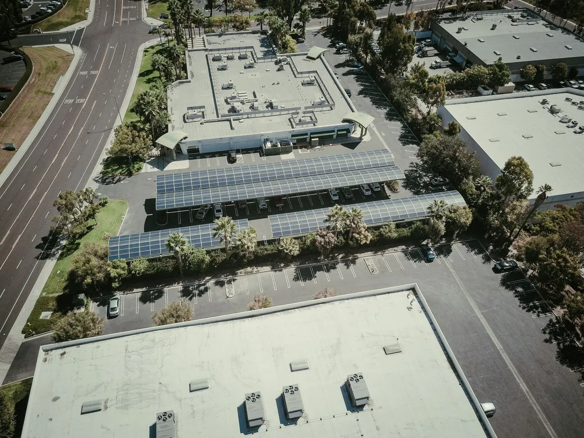 Aerial view of commercial building with rooftop solar panel arrays and parking lot with charging infrastructure