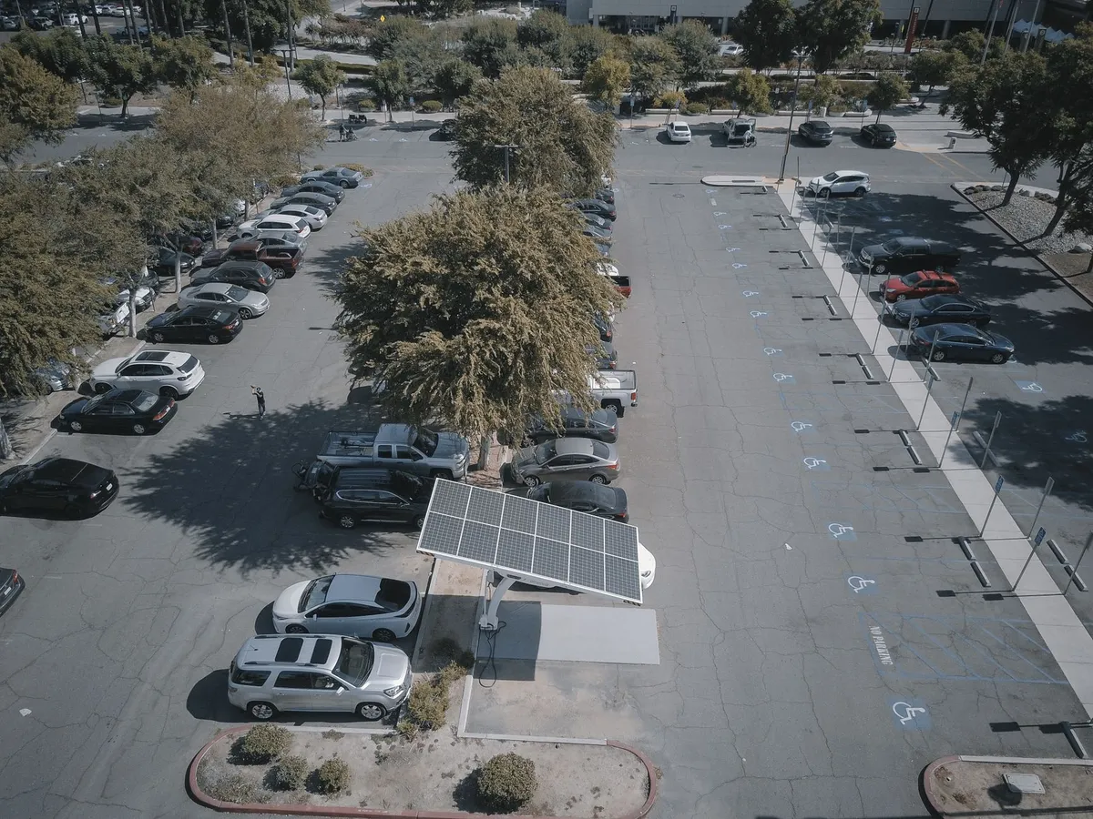 Aerial view of EV charging depot with solar panel canopy, multiple charging stations, and parked electric vehicles in spacious lot with trees