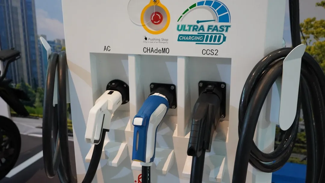 Electric vehicle charging station display showing three charging connector types labeled AC, CHAdeMO, and CCS2 with corresponding white, blue, and black connectors.