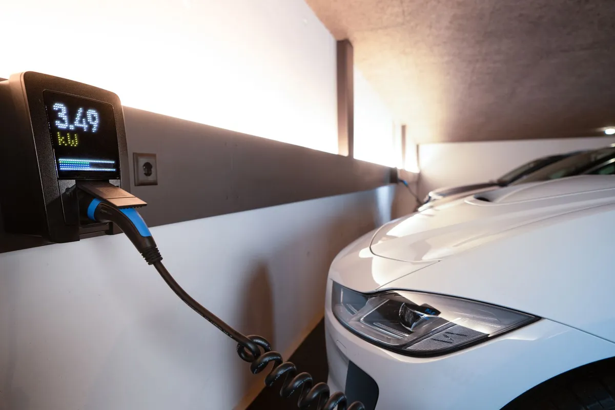 Wall-mounted EV charger with digital display showing 3.4kW output and blue charging cable next to white electric car