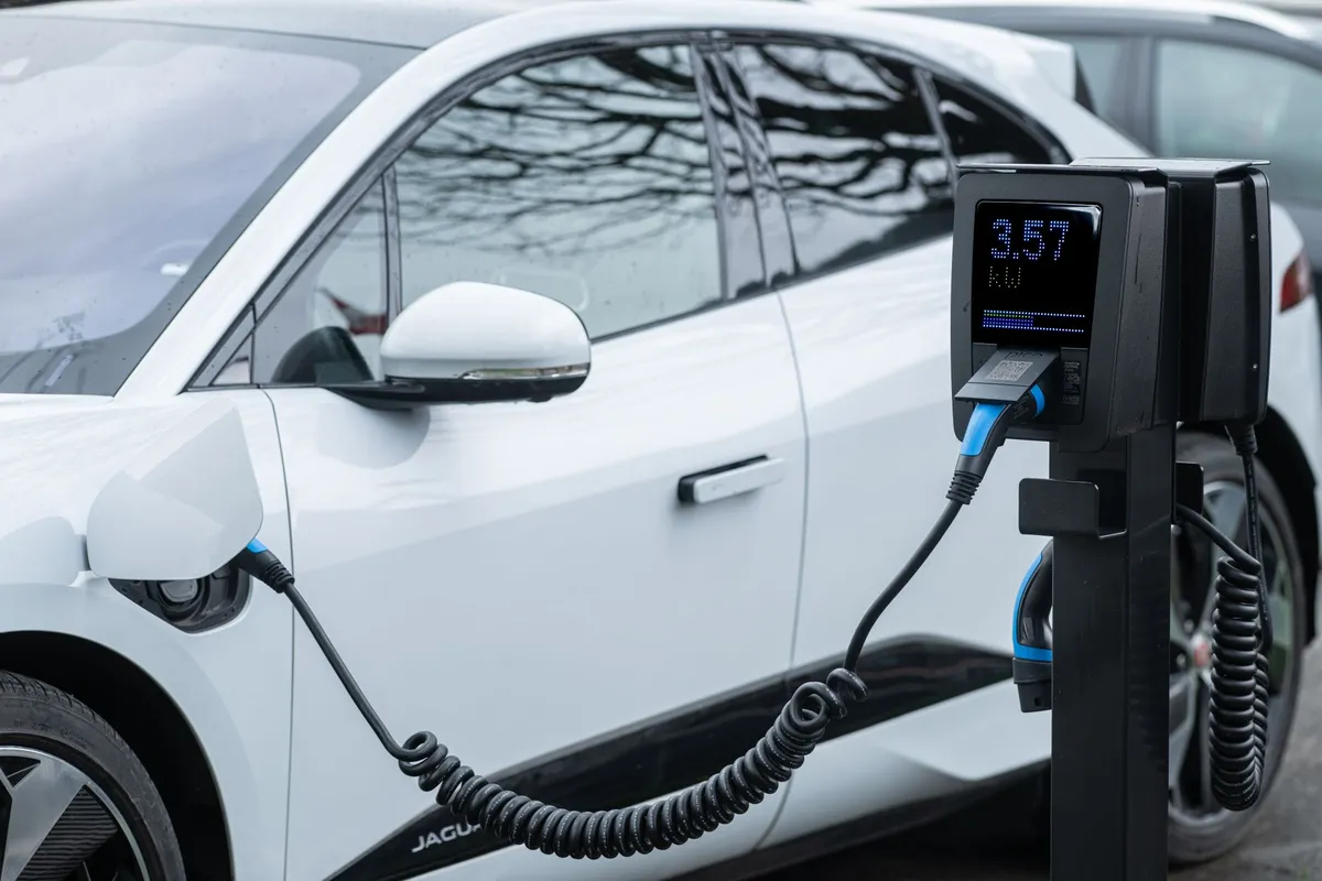 White electric vehicle charging at home charging station with digital display showing kWh, coiled cable connected to vehicle port