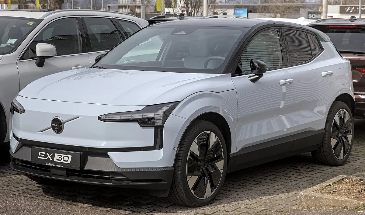 White Volvo EX30 electric SUV parked at a dealership, showing front three-quarter view with distinctive LED headlights and modern design
