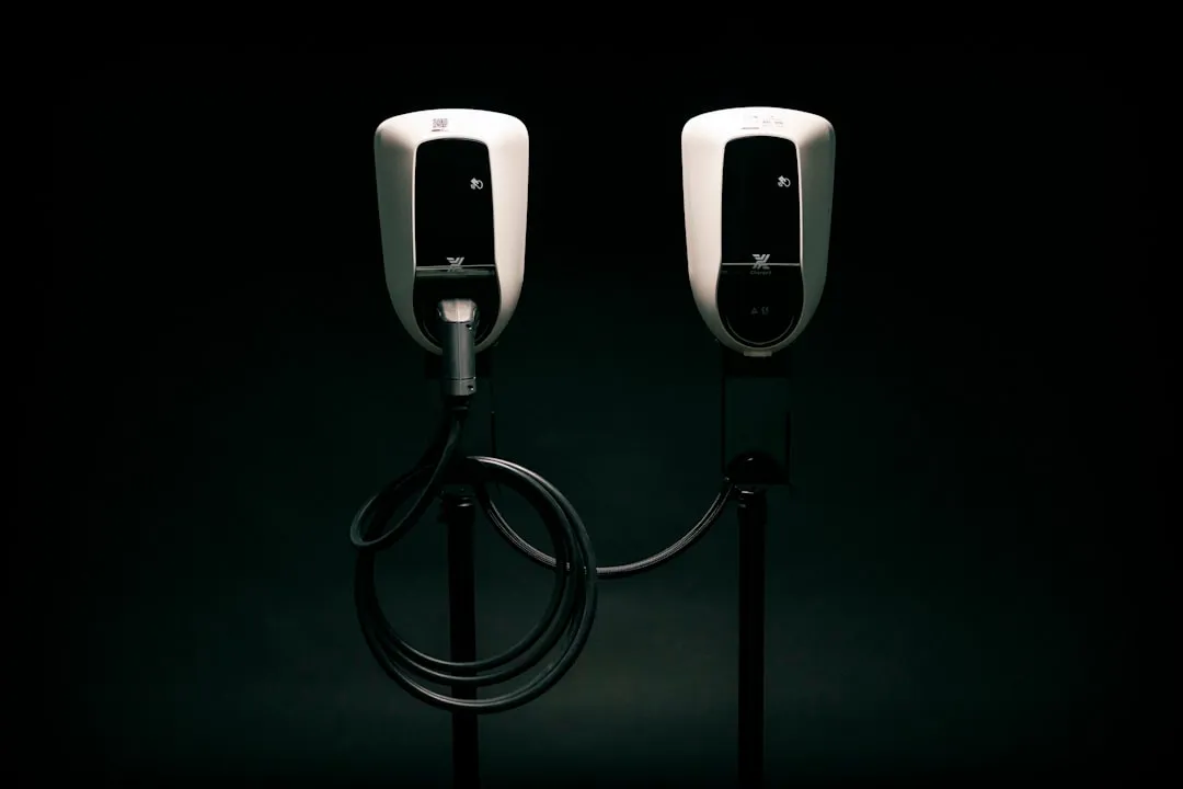 Two white electric vehicle charging stations with black display screens against dark background