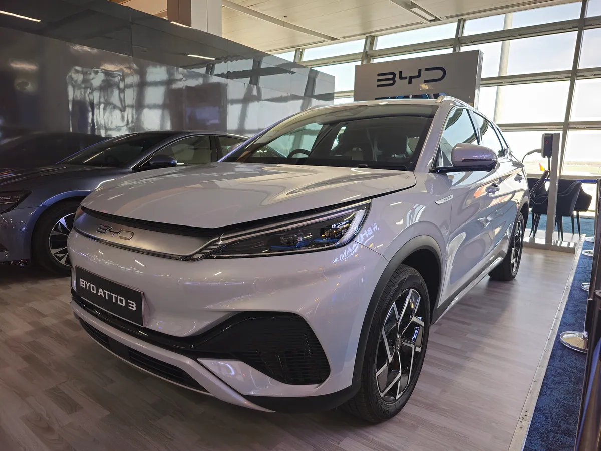 White BYD Atto 3 electric SUV displayed in a showroom with floor-to-ceiling windows and BYD signage overhead