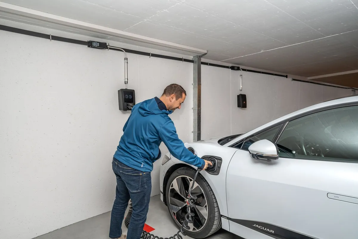Man plugging EV charging cable into white Jaguar electric vehicle in residential garage with wall-mounted charger