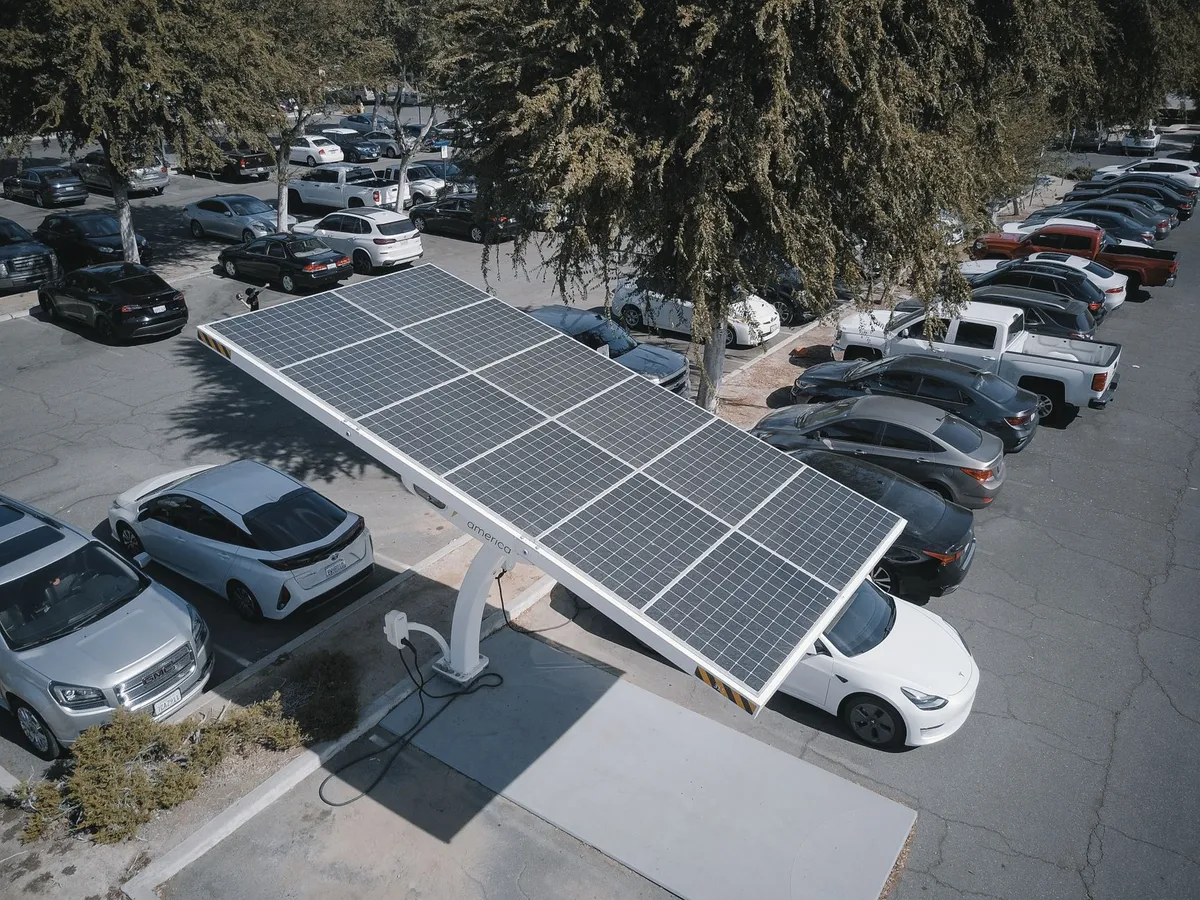 Solar panel canopy with EV charger in parking lot surrounded by parked vehicles and trees