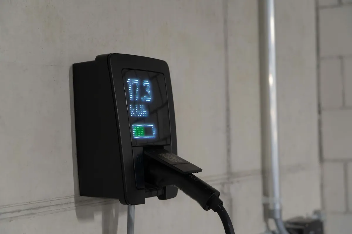 Black wall-mounted EV charging unit with LED display mounted on white residential garage wall