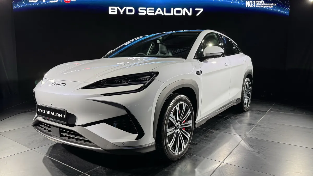 White BYD Sealion 7 electric SUV on display at a showroom with blue lighting backdrop