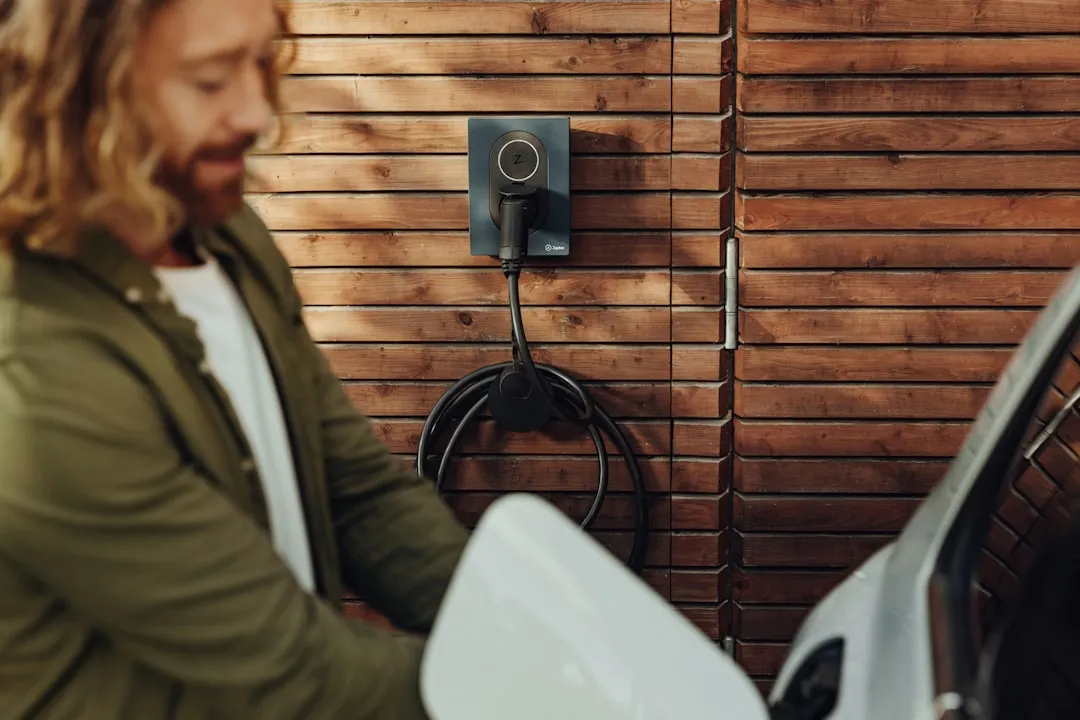 Wall-mounted EV charger on wooden residential exterior with coiled black charging cable below