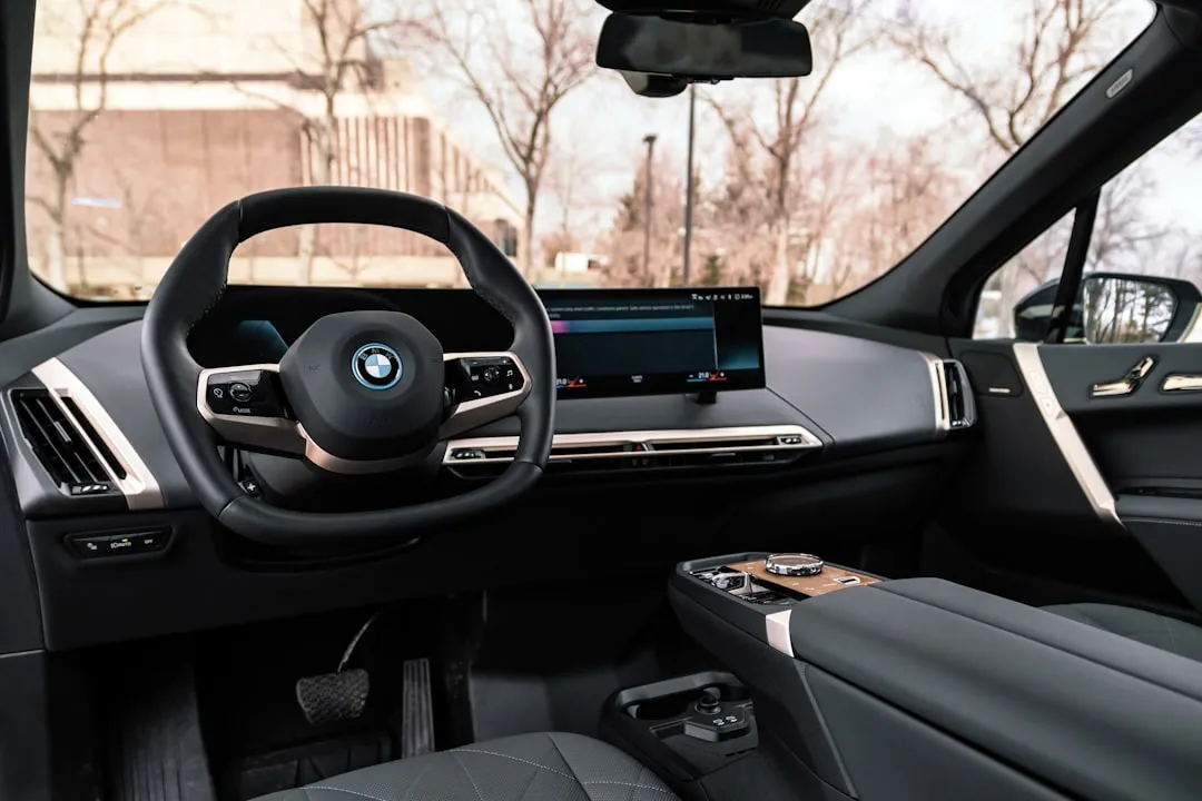 BMW electric vehicle interior showing curved iDrive display, digital instrument cluster, and premium dashboard with panoramic glass roof