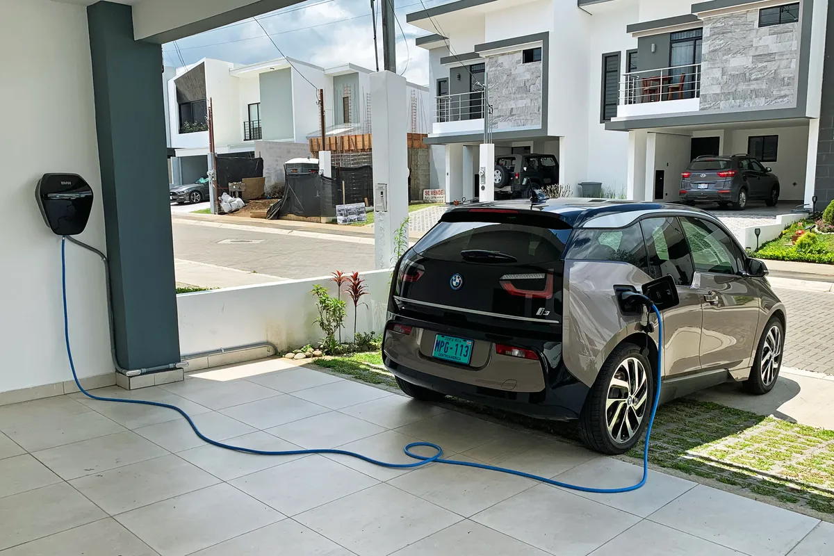A blue Type-2 cable runs from a home wallbox to a BMW i3 parked in a garage